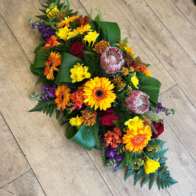 Autumn Tribute - Honour a loved one with the rich colours of autumn in this vibrant funeral arrangement. Featuring warm orange, red, and yellow blooms, this tribute brings a touch of seasonal beauty to commemorative events, providing a heartfelt expression of remembrance.